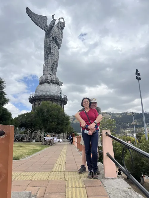 A man hugging his wife from behind with the Virgin of Quito in the background